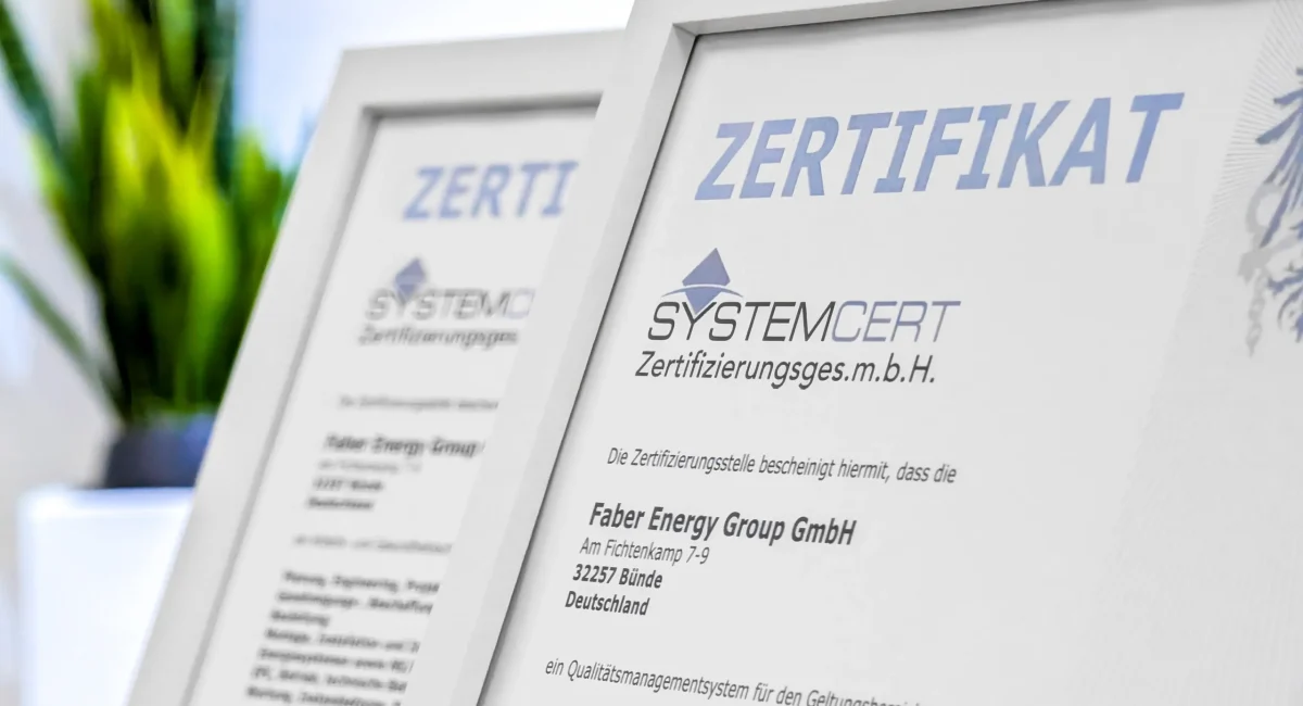 Zwei gerahmte Zertifikate der SystemCERT Zertifizierungsges.m.b.H. für die Faber Energy Group GmbH in Bünde, im Vordergrund gut sichtbar das Zertifikat für das Qualitätsmanagementsystem